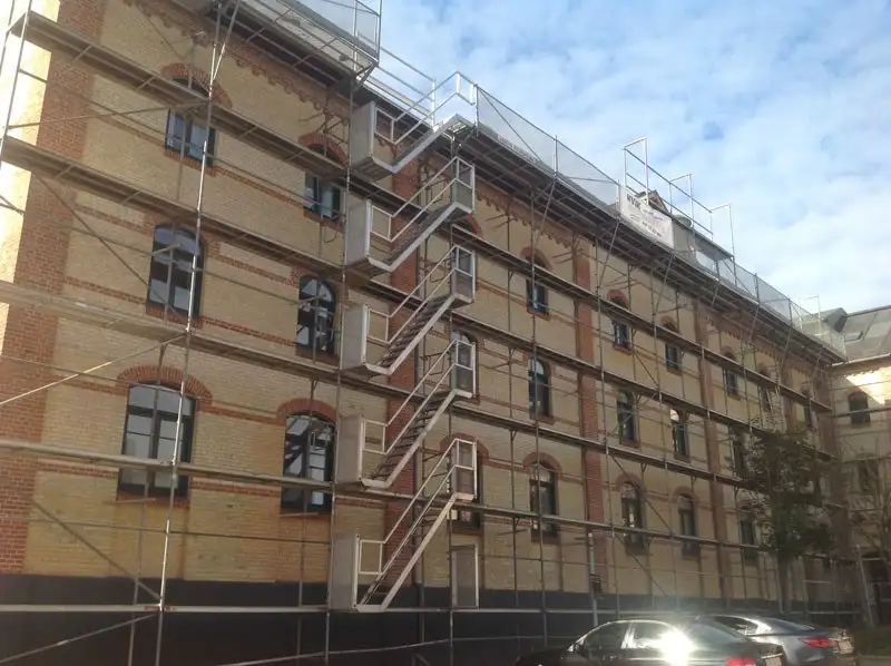 Stor murstensbygning med stillads under tagrenovering